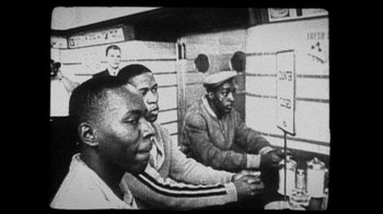 Movie still from “13th” (2016), directed by Ava DuVernay – A group of men sitting in front of a window; Medium shot, High angle