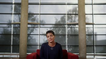 Movie still from “13th” (2016), directed by Ava DuVernay – A woman sitting on a red chair in front of a window; Medium shot, Low angle