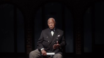Movie still from “13th” (2016), directed by Ava DuVernay – An older man sitting in a chair in front of a brick wall; Medium shot, Low angle