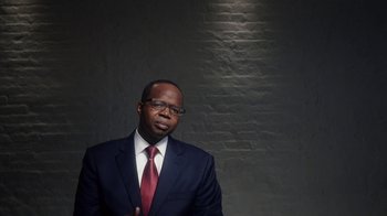 Movie still from “13th” (2016), directed by Ava DuVernay – A man in a suit and tie standing in front of a brick wall; Close Up shot, Over the shoulder angle
