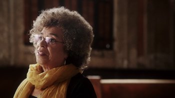 Movie still from “13th” (2016), directed by Ava DuVernay – An older woman wearing glasses and a yellow scarf; Close Up shot, Over the shoulder angle