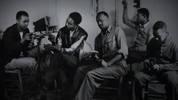 Movie still from “13th” (2016), directed by Ava DuVernay – A black and white photo of two men sitting in a room; Medium shot, High angle