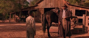 Movie still from “Rosewood” (1997), directed by John Singleton – Two men and a boy standing next to a brown horse; Medium shot, Over the shoulder angle