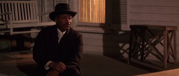 Movie still from “Rosewood” (1997), directed by John Singleton – A man sitting on the ground wearing a hat; Medium shot, Over the shoulder angle
