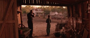 Movie still from “Rosewood” (1997), directed by John Singleton – Two men standing in a dirt field near a building; Extreme Wide shot, Over the shoulder angle