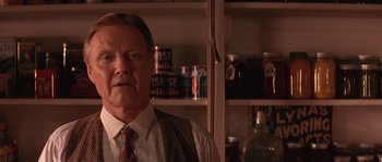 Movie still from “Rosewood” (1997), directed by John Singleton – A man in a suit and tie in front of shelves; Close Up shot, Low angle
