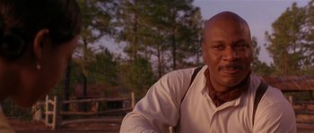 Movie still from “Rosewood” (1997), directed by John Singleton – A man sitting in front of a forest; Close Up shot, Low angle