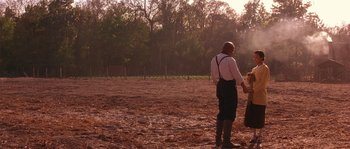 Movie still from “Rosewood” (1997), directed by John Singleton – A man and a child in a field holding hands; Wide shot, Over the shoulder angle