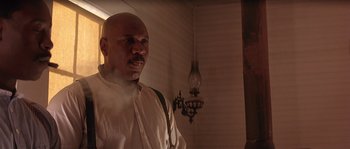 Movie still from “Rosewood” (1997), directed by John Singleton – A bald man in a white dress shirt and suspenders; Medium shot, Low angle