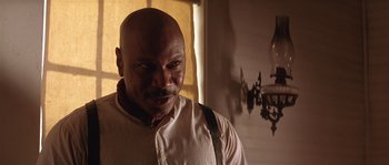 Movie still from “Rosewood” (1997), directed by John Singleton – A bald man with a black eye stares into the camera; Close Up shot, Low angle