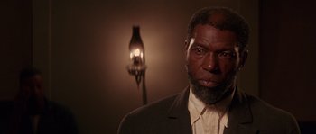Movie still from “Rosewood” (1997), directed by John Singleton – A man in a suit and tie in front of a lamp; Close Up shot, Low angle