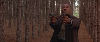 Movie still from “Rosewood” (1997), directed by John Singleton – A man holding two pistols while standing next to a forest; Medium shot, Low angle