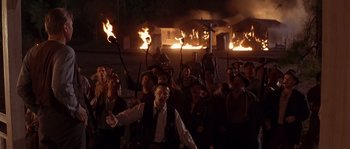 Movie still from “Rosewood” (1997), directed by John Singleton – A group of people holding torches in front of a fire; Wide shot, High angle