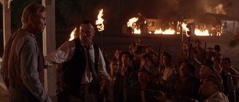 Movie still from “Rosewood” (1997), directed by John Singleton – A group of people holding torches in front of a fire; Medium shot, High angle