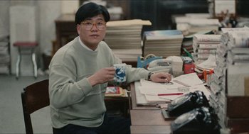 Movie still from “Rouge” (1987), directed by Stanley Kwan – A man sitting at a desk holding a coffee mug; Medium shot, High angle
