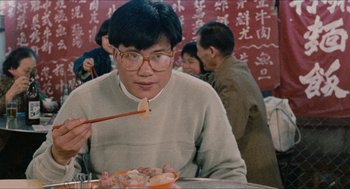 Movie still from “Rouge” (1987), directed by Stanley Kwan – A man sitting at a table with chopsticks in front of him; Medium shot, Over the shoulder angle