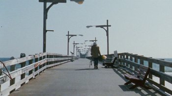 Movie still from “Ruby in Paradise” (1993), directed by Victor Nunez – A person walking across a bridge holding a camera; Extreme Wide shot, High angle