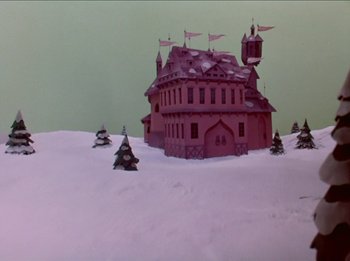 Movie still from “Rudolph the Red-Nosed Reindeer” (1964), directed by Larry Roemer – A pink house with a bunch of trees in the snow; Extreme Wide shot, Low angle