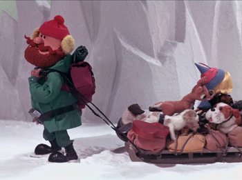 Movie still from “Rudolph the Red-Nosed Reindeer” (1964), directed by Larry Roemer – A gnome and a dog pulling a sled in the snow; Wide shot, High angle