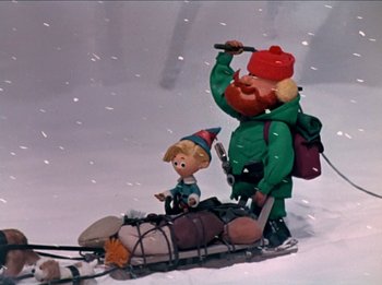 Movie still from “Rudolph the Red-Nosed Reindeer” (1964), directed by Larry Roemer – A couple of figurines sitting on top of a sled in the snow; Medium shot, Low angle