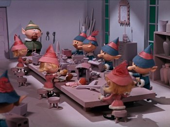 Movie still from “Rudolph the Red-Nosed Reindeer” (1964), directed by Larry Roemer – A group of people sitting at a table with a lot of toys; Wide shot, High angle