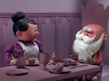 Movie still from “Rudolph the Red-Nosed Reindeer” (1964), directed by Larry Roemer – A couple of statues sitting on top of a wooden table; Medium shot, Over the shoulder angle