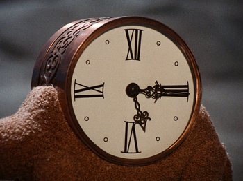 Movie still from “Rudolph's Shiny New Year” (1976), directed by Jules Bass – A clock with roman numerals on top of a pile of sand; Extreme Close Up shot, Overhead angle
