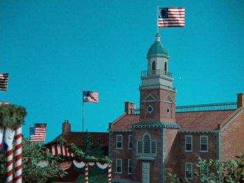 Movie still from “Rudolph's Shiny New Year” (1976), directed by Jules Bass – A building with a clock tower in the middle of it and american flags flying in the background; Extreme Wide shot, High angle