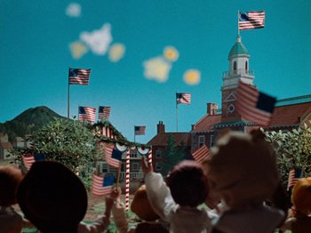 Movie still from “Rudolph's Shiny New Year” (1976), directed by Jules Bass – A group of people standing in front of a clock tower with american flags flying; Medium shot, Low angle