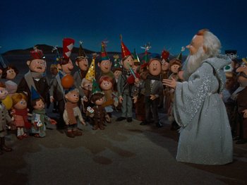 Movie still from “Rudolph's Shiny New Year” (1976), directed by Jules Bass – A group of people gathered around a statue of a wizard; Wide shot, High angle