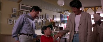 Movie still from “Rumble in the Bronx” (1995), directed by Stanley Tong – Two men and a boy are holding hands in a room; Medium shot, Over the shoulder angle