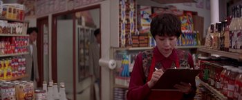 Movie still from “Rumble in the Bronx” (1995), directed by Stanley Tong – A person writing on a piece of paper in a store; Medium shot, Over the shoulder angle