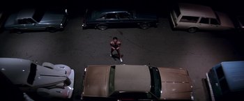 Movie still from “Rumble in the Bronx” (1995), directed by Stanley Tong – A man standing on the side of a road next to parked cars; Wide shot, Overhead angle