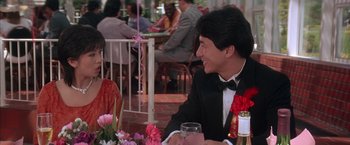 Movie still from “Rumble in the Bronx” (1995), directed by Stanley Tong – A man sitting at a table in front of a glass of wine; Medium shot, Over the shoulder angle