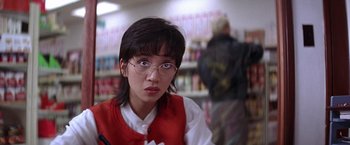 Movie still from “Rumble in the Bronx” (1995), directed by Stanley Tong – A woman in a red vest and glasses in front of a book shelf; Close Up shot, Over the shoulder angle