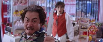 Movie still from “Rumble in the Bronx” (1995), directed by Stanley Tong – A man holding a large knife in front of a woman; Close Up shot, Low angle