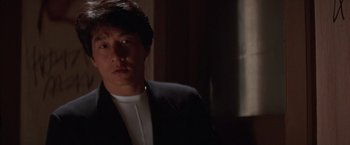 Movie still from “Rumble in the Bronx” (1995), directed by Stanley Tong – A man wearing a suit and tie in a room; Close Up shot, Over the shoulder angle