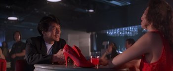 Movie still from “Rumble in the Bronx” (1995), directed by Stanley Tong – A man sitting at a table next to a pair of red high heels; Medium shot, Low angle