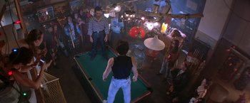 Movie still from “Rumble in the Bronx” (1995), directed by Stanley Tong – A group of people standing around a pool table in a room; Wide shot, High angle