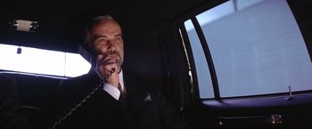 Movie still from “Rumble in the Bronx” (1995), directed by Stanley Tong – A man sitting in the back seat of a car talking on a phone; Close Up shot, Low angle