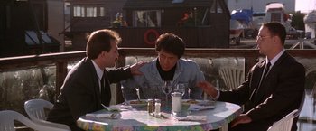 Movie still from “Rumble in the Bronx” (1995), directed by Stanley Tong – Two men sitting at an outdoor table with a glass of wine; Medium shot, Over the shoulder angle