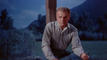 Movie still from “Run for Cover” (1955), directed by Nicholas Ray – An older man sitting on the ground in front of trees; Medium shot, Low angle