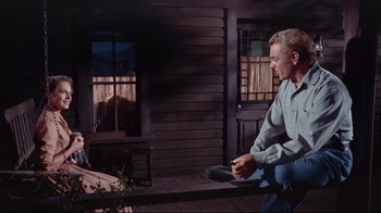 Movie still from “Run for Cover” (1955), directed by Nicholas Ray – A man sitting on a bench in front of a wooden house; Wide shot, Low angle