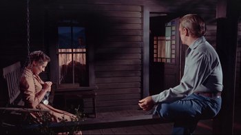 Movie still from “Run for Cover” (1955), directed by Nicholas Ray – A man sitting on a bench in front of a wooden house; Wide shot, Low angle
