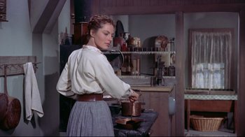 Movie still from “Run for Cover” (1955), directed by Nicholas Ray – A woman in a white shirt and a brown skirt is cooking; Medium shot, Over the shoulder angle