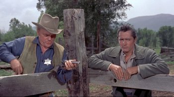Movie still from “Run for Cover” (1955), directed by Nicholas Ray – Two men in cowboy garb are standing next to a wooden fence; Medium shot, Over the shoulder angle