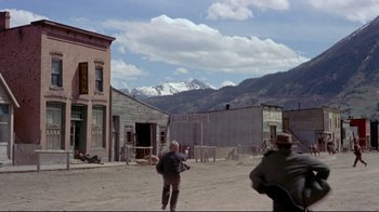 Movie still from “Run for Cover” (1955), directed by Nicholas Ray – A man in a cowboy hat is standing in the middle of a dirt road; Extreme Wide shot, Over the shoulder angle