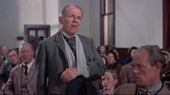 Movie still from “Run for Cover” (1955), directed by Nicholas Ray – An older man wearing a suit and tie in front of an audience; Medium shot, Over the shoulder angle