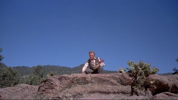 Movie still from “Run for Cover” (1955), directed by Nicholas Ray – A man sitting on top of a rock on top of a hill; Wide shot, Low angle