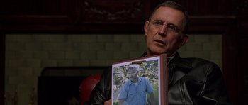 Movie still from “Runaway Jury” (2003), directed by Gary Fleder – A man holding up a picture of himself; Close Up shot, Over the shoulder angle